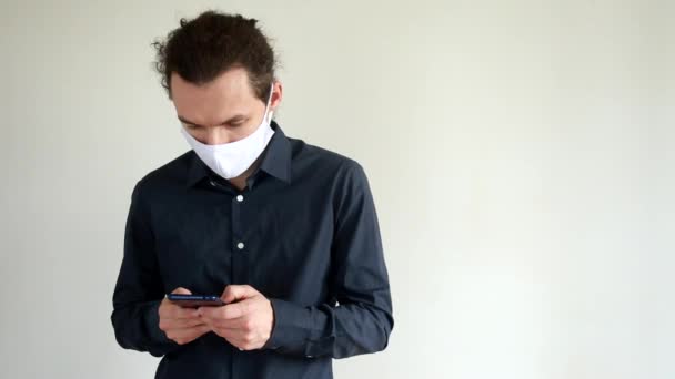 Muž v ochranné lékařské masce používající smartphone. Komunikace a práce online během pandemie koronaviru. — Stock video