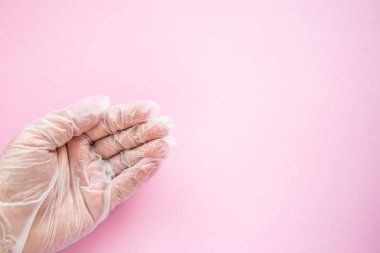 Kadın eli şeffaf bir tıbbi eldiven giymiş. Avuç içi pembe arka planda. Jest istiyorum. Bağışlar ve doktorlara zamanında koronovirüs salgını konsepti.