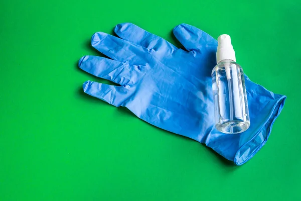 Hand picked sanitizer and blue medical glove as protection against coronavirus on green background — Stock Photo, Image