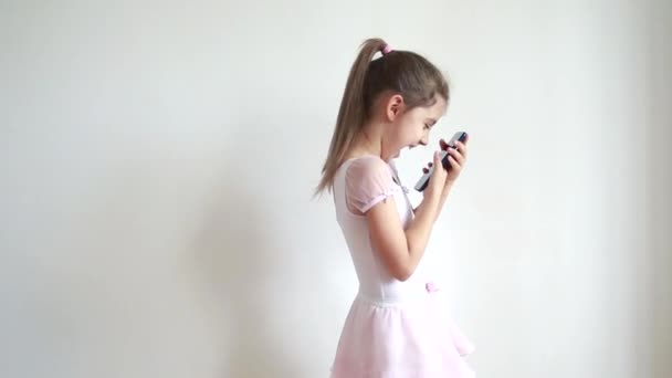 Klein emotioneel blank meisje kijkt naar de telefoon en lacht veel, selfies nemen en poseren voor foto 's, chatten met vrienden online. Online communicatie en blogging concept. — Stockvideo