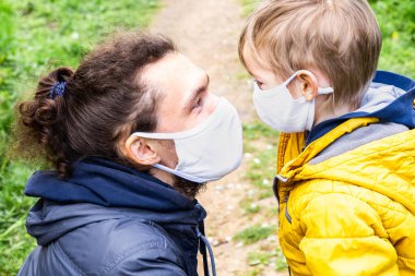 Koronavirüs salgını sırasında aile koruması. Baba ve oğul koruyucu maskeler takmış, alnından birbirlerine bakıyorlar. COVID-19 sırasındaki aile bakımı ve birliktelik.
