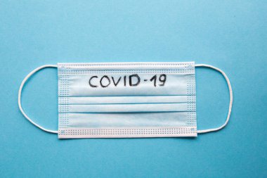 Mavi arkaplanda COVID 19 yazısıyla üst görünüm tıbbi maske düzeni.
