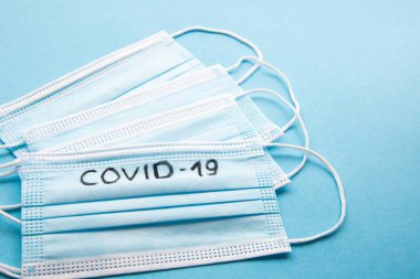 Mavi arka planda COVID-19 yazılı birkaç tıbbi yüz maskesi var. Coronavirus enfeksiyonu önleme konsepti