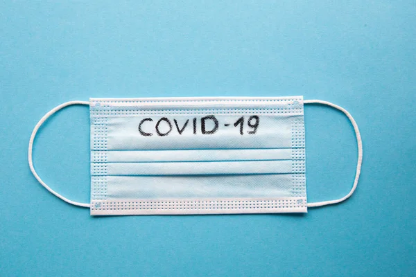 Top view medical face mask layout with inscription COVID-19 on a blue background.
