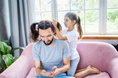 Babalar Günü konsepti. Sevimli küçük kız babasına neşeli bir saç stili yapıyor. Mutlu çocukluk ve harika ilişkiler. Baba ve kızı birlikte vakit geçiriyorlar. Mutlu aile evde kalıyor..