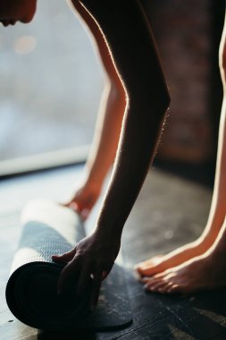Bir kız elleriyle halı sarar ve ayak parmaklarının üzerinde durur. Yoga için bir spor salonunda ya da güneşli bir havada evde.