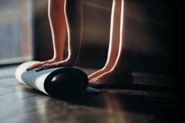 Bir kız elleriyle halı sarar ve ayak parmaklarının üzerinde durur. Yoga için bir spor salonunda ya da güneşli bir havada evde.