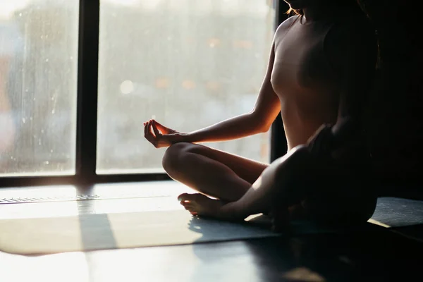 Girl sitting on a yoga mat in lotus position. sunlight from the window to the studio — Stock Photo, Image