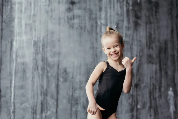 Souriant fille gymnaste posant près d'un mur texturé noir . — Photo