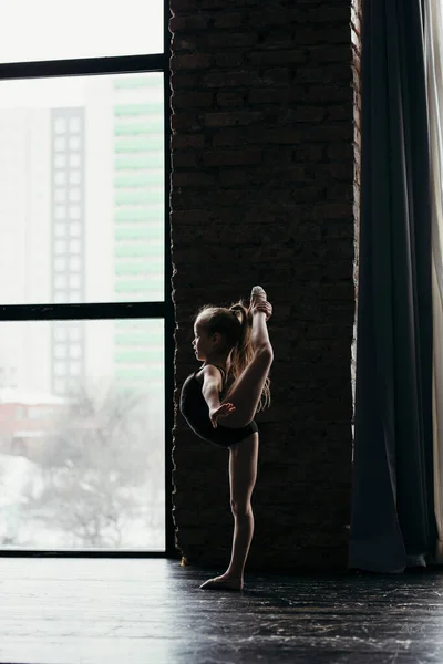 Gymnast stands on one leg near the window. Silhouette of a girl — Stockfoto