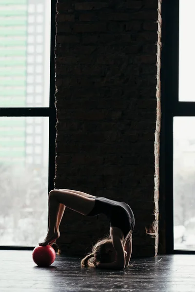 The girl does gymnastics with a red ball near the window. — Stockfoto