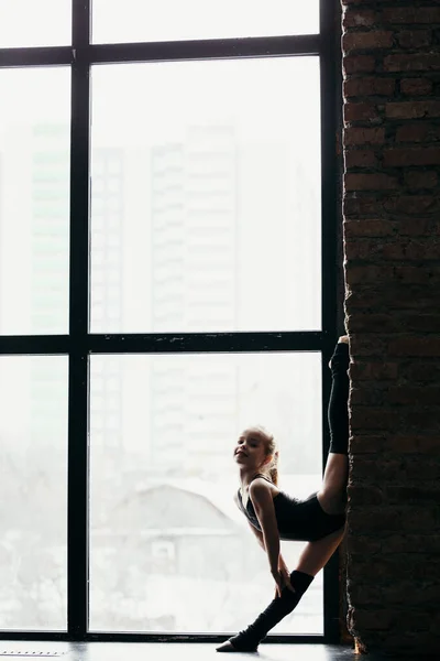 Gymnast στέκεται στο ένα πόδι κοντά στο παράθυρο. Σιλουέτα ενός κοριτσιού σε φωτεινό φόντο. — Φωτογραφία Αρχείου