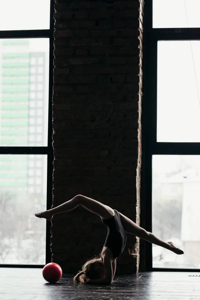 La fille fait de la gymnastique avec une balle rouge près de la fenêtre. Silhouette sur un fond lumineux . — Photo
