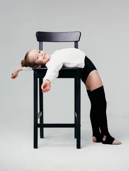 Гімнастка дівчина позує сидячи на стільці на білій стіні . — стокове фото
