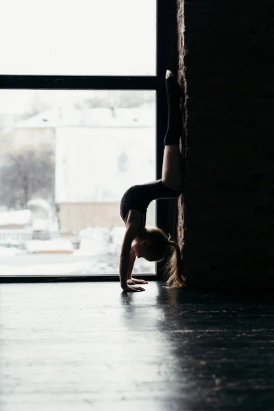 La gymnaste se tient dans ses bras. Silhouette d'une fille sur un fond de fenêtre lumineux . — Photo