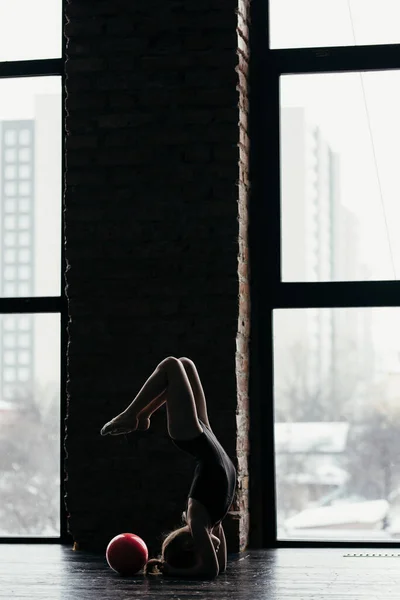 Das Mädchen turnt mit einem roten Ball am Fenster herum. Silhouette auf hellem Hintergrund. — Stockfoto