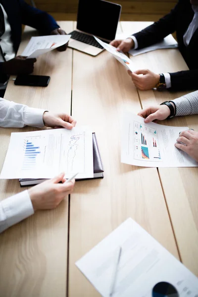 Hands of four businessmen of different nationalities with charts of company subsidiaries — Stockfoto