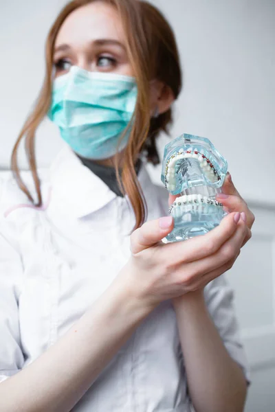 Un bel dentista con una maschera blu tiene una falsa mascella blu con l'apparecchio dentale sui denti — Foto Stock