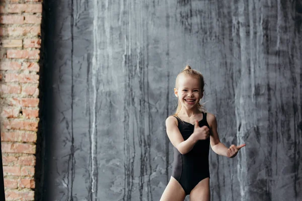 Souriant fille gymnaste posant près d'un mur texturé noir . — Photo