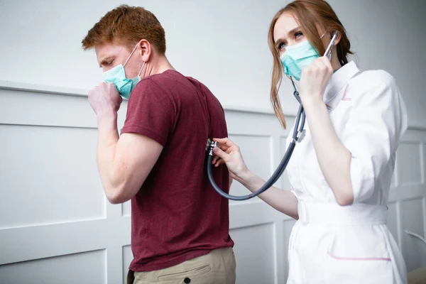 Um médico estagiário bonito diagnostica um paciente. Paciente reclama ao médico bonito sobre tosse e mal-estar — Fotografia de Stock