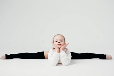 Jimnastikçi kız beyaz bir duvara karşı sicim üzerinde oturuyor..