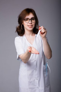 Genç kadın doktor, muayene aletleriyle hastaya dilini nasıl çıkaracağını gösteriyor.