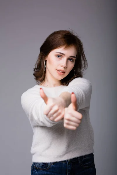 Πολύ ελκυστική κοπέλα με ελαφρύ σακάκι δείχνει τους αντίχειρες. Γυναίκα δείχνει σαν σημάδι και εντάξει με τα χέρια της και κοιτάζει την κάμερα — Φωτογραφία Αρχείου