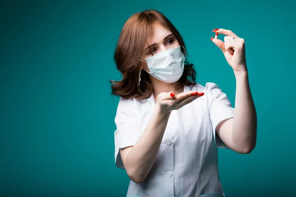 Close-up muito médico especialista em uma máscara azul detém uma pílula que é a cura para um novo vírus desconhecido — Fotografia de Stock