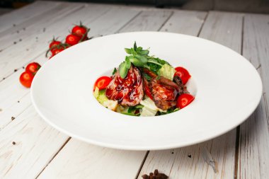 Büyük yuvarlak beyaz tabakta servis edilen et ve barbekü soslu sebze salatası. Ahşap arka planda bir restoran yemeği..