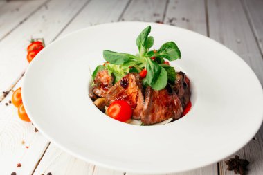 Büyük yuvarlak beyaz tabakta servis edilen et ve barbekü soslu sebze salatası. Ahşap arka planda bir restoran yemeği..