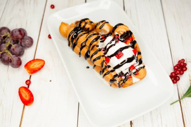 Beyaz tabakta iştah açıcı tatlı. Masanın üzerinde çilek ve üzümlerle süslenmiş bir restoran yemeği..