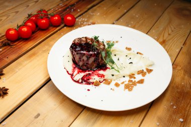 Sulu ızgara biftek, kırmızı soslu patates püresinin üzerinde yatıyor. Bir demet kirazlı domates ve yıldız anasonunun yanında..