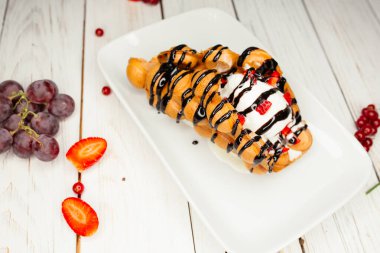 Beyaz tabakta iştah açıcı tatlı. Masanın üzerinde çilek ve üzümlerle süslenmiş bir restoran yemeği..