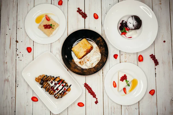 Conjunto de postres dulces sobre fondo de madera. El plato del restaurante en la mesa está decorado con fresas y uvas . — Foto de Stock