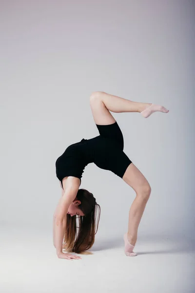 Krásná gymnastka v černém sportovním oblečení stojící na jeho rukou na bílém pozadí. Sportovní dívka dělá handstand. — Stock fotografie