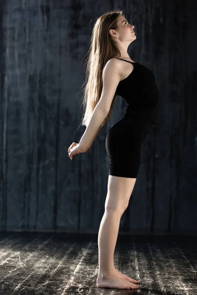 Перед виконанням вправ одна європейка в чорному одязі стоїть на стійці і тягне спину, щоб розігрітися. — стокове фото