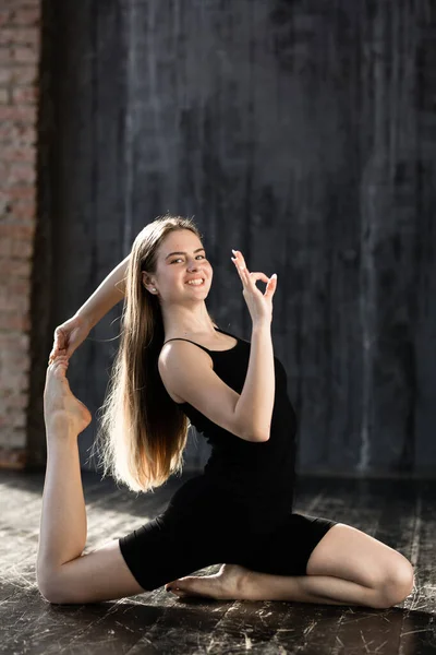 Молода дівчина в чорному спортивному одязі робить йогу і показує знак добре, тому що йога не складна — стокове фото