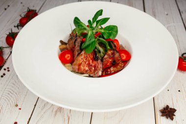 Büyük yuvarlak beyaz tabakta servis edilen et ve barbekü soslu sebze salatası. Ahşap arka planda bir restoran yemeği..