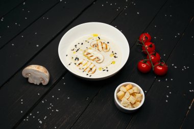 Siyah ahşap bir masada, üzerinde deniz tuzu serpiştirilmiş koyu beyaz bir tabakta servis edilen lezzetli mantar kreması çorbası..