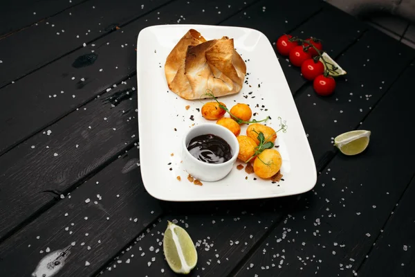Hornear servido con salsa oscura en un plato rectangular blanco. Sobre el fondo de una mesa de madera negra decorada con tomates cherry y rodajas de limón . — Foto de Stock