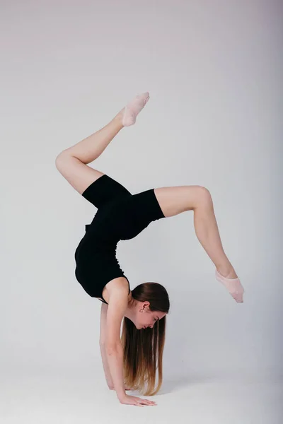 Piękny gimnastyk w czarnej odzieży sportowej stojący na rękach na białym tle. Sportowa dziewczyna robi na rękach. — Zdjęcie stockowe
