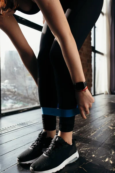 身穿黑色运动服的女运动员拉着橡皮筋锻炼腿肌肉 — 图库照片