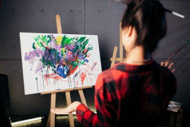 Ressam sehpanın önündeki stüdyoda ve yeni soyut suluboya resme bakıyor. Arkadaki kırmızı gömlekli kız..