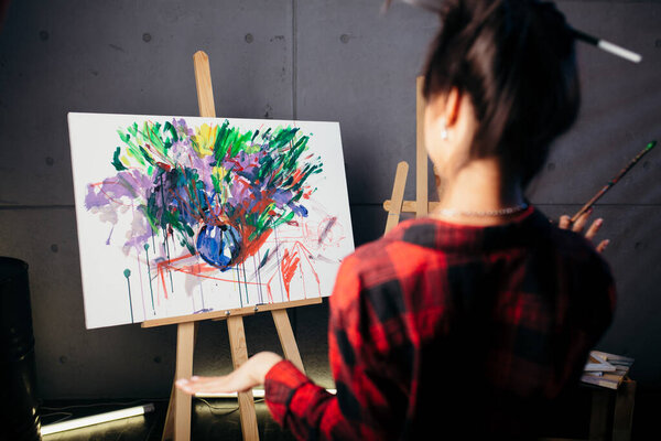 The artist is in the Studio in front of the easel and looks at the new abstract watercolor color painting. The girl in the red shirt from the back.