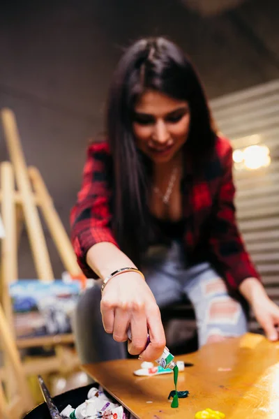 Brunette artist mixes paint on a wooden palette near the easel and painted with acrylic paint painting. — Stock Photo, Image