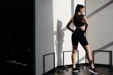 Şişirilmiş kadın, siyah spor giyim kuşağında güneşin altında beyaz bir arka planda kamera karşısında duruyor..