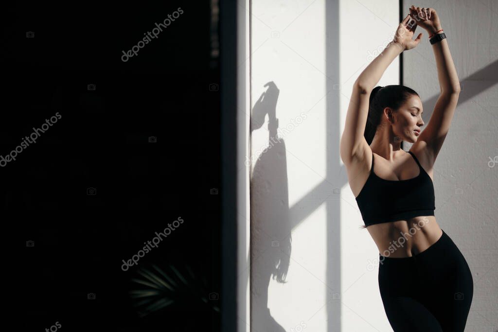 Athletic girl in black sportswear standing under the rays of the sun. Natural light during training