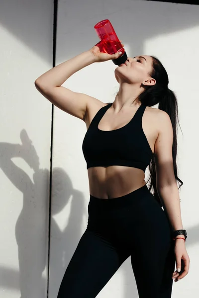 Attractive woman In sports wear drinking water after workout. Playing sports at home.