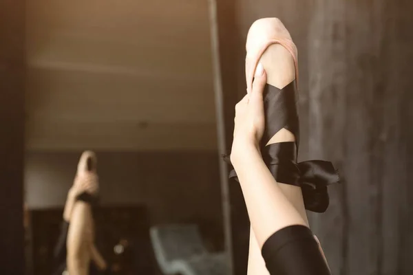Een close-up. De danser trekt het been omhoog in Pointe schoenen. Roze Pointe schoenen met zwarte linten op het been. — Stockfoto
