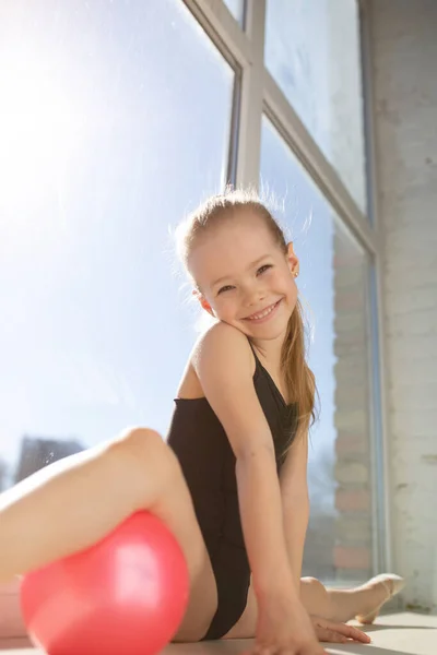 Le jeune gymnaste effectue un échauffement matinal avant la compétition. La fille a fait les fentes sous le pied par la boule rose . — Photo